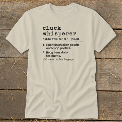 Cream t-shirt with black text defining "cluck whisperer" for chicken lovers.