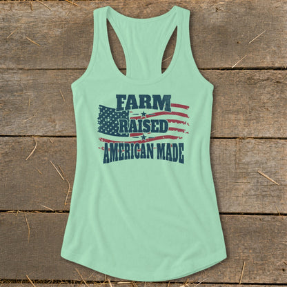 Light mint green racerback tank top with "FARM RAISED AMERICAN MADE" text over American flag graphic.