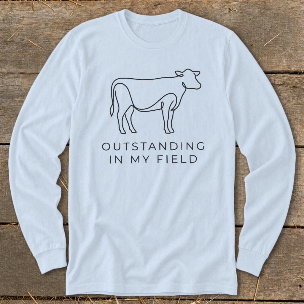 Light blue long-sleeve shirt with a line drawing of a cow and text "OUTSTANDING IN MY FIELD".