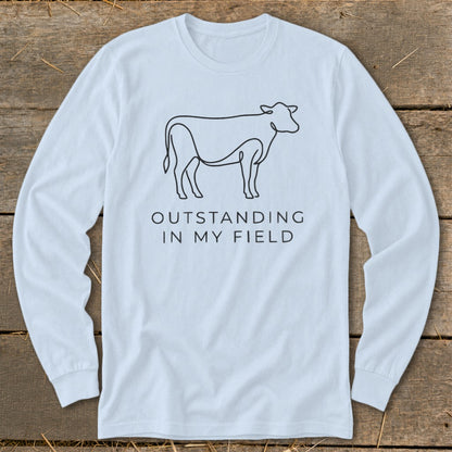 Light blue long-sleeve shirt with a line drawing of a cow and text "OUTSTANDING IN MY FIELD".