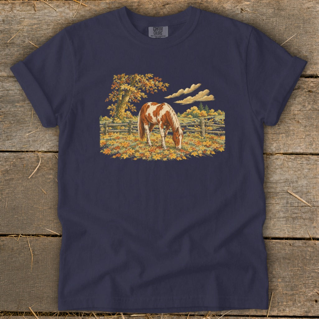 Navy t-shirt with a painting of a brown and white horse grazing in a field of fall leaves.