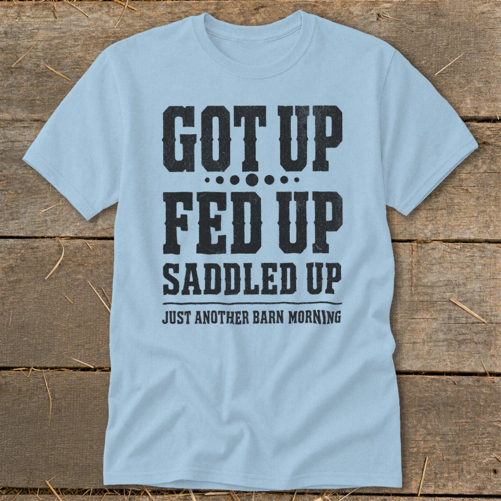 Light blue t-shirt with black text that reads "GOT UP FED UP SADDLED UP JUST ANOTHER BARN MORNING."