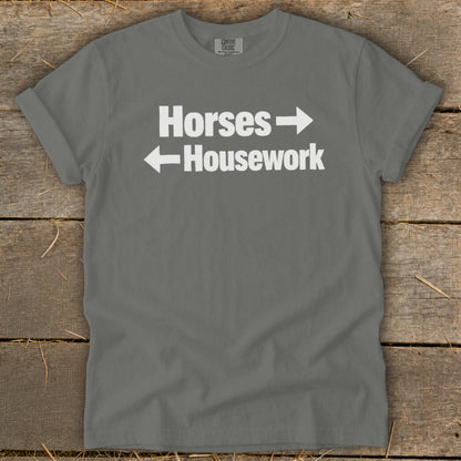 A dark gray t-shirt with white text reading Horses with a right arrow and Housework with a left arrow.