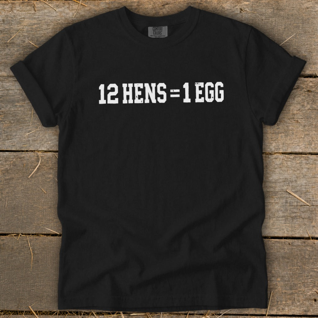 Black t-shirt featuring the white distressed text 12 HENS = 1 EGG, laid flat on wooden boards.