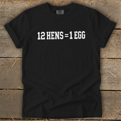 Black t-shirt featuring the white distressed text 12 HENS = 1 EGG, laid flat on wooden boards.
