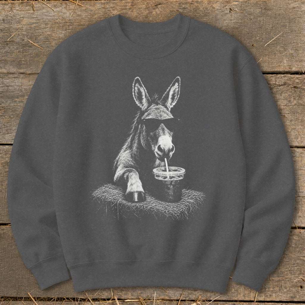 Donkey wearing sunglasses drinks from a cup with a straw on hay.