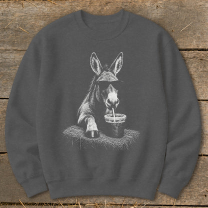 Donkey wearing sunglasses drinks from a cup with a straw on hay.