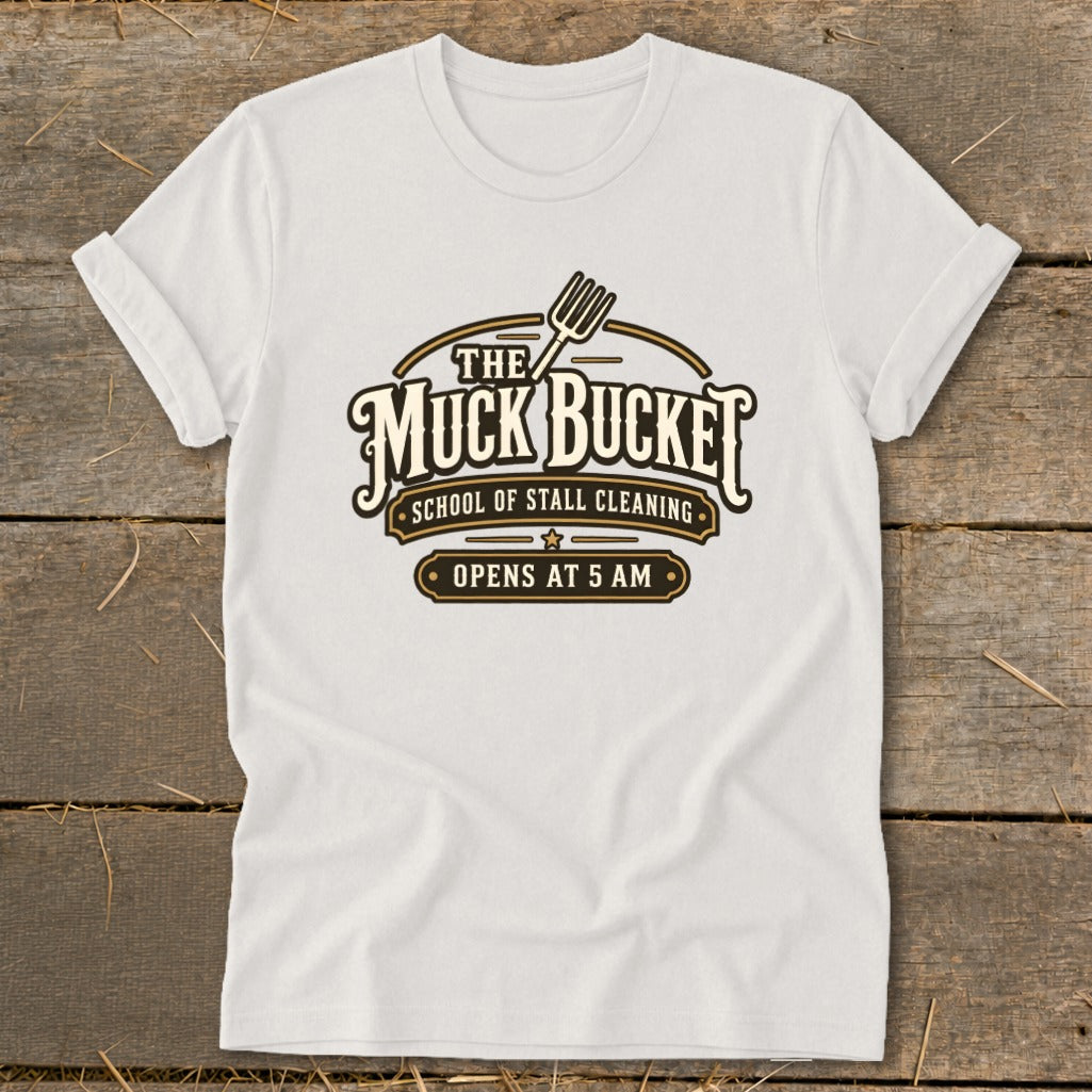White t-shirt with "The Muck Bucket School of Stall Cleaning Opens at 5 AM" logo.
