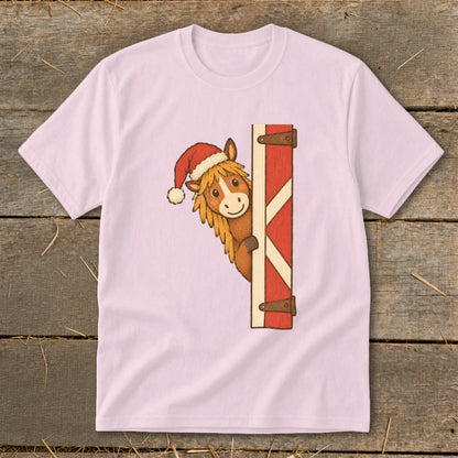 Pink t-shirt with a cartoon horse wearing a Santa hat peeking around a red barn door.
