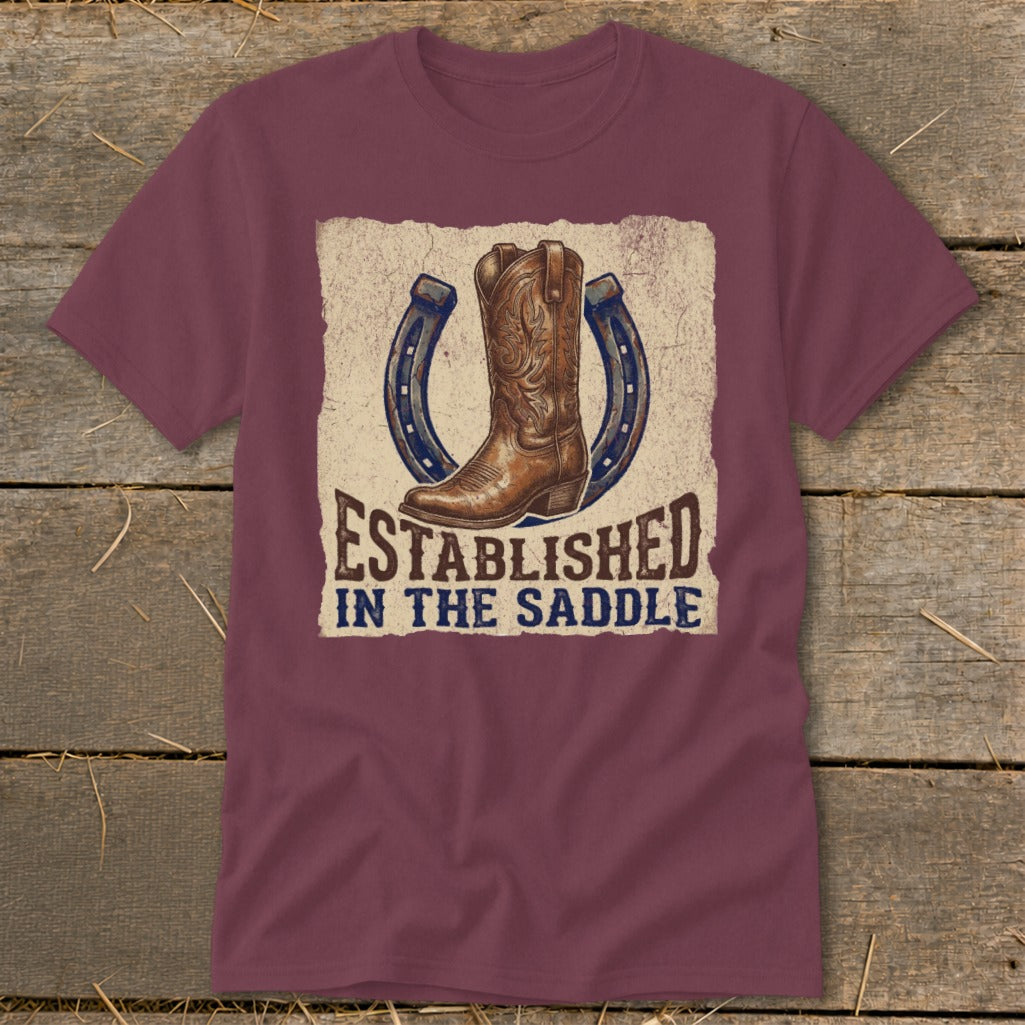 Maroon t-shirt with a cowboy boot and two horseshoes graphic, text reads "Established in the Saddle".