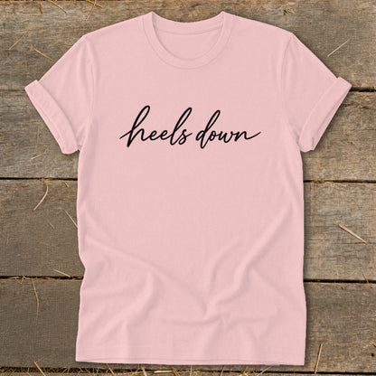 Pink t-shirt with black cursive text that says "heels down".