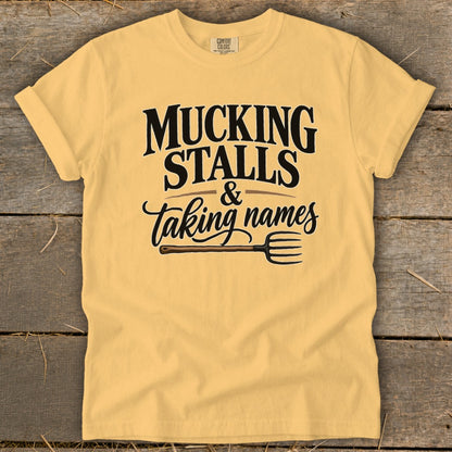 Yellow t-shirt with "MUCKING STALLS & taking names" and a pitchfork graphic.