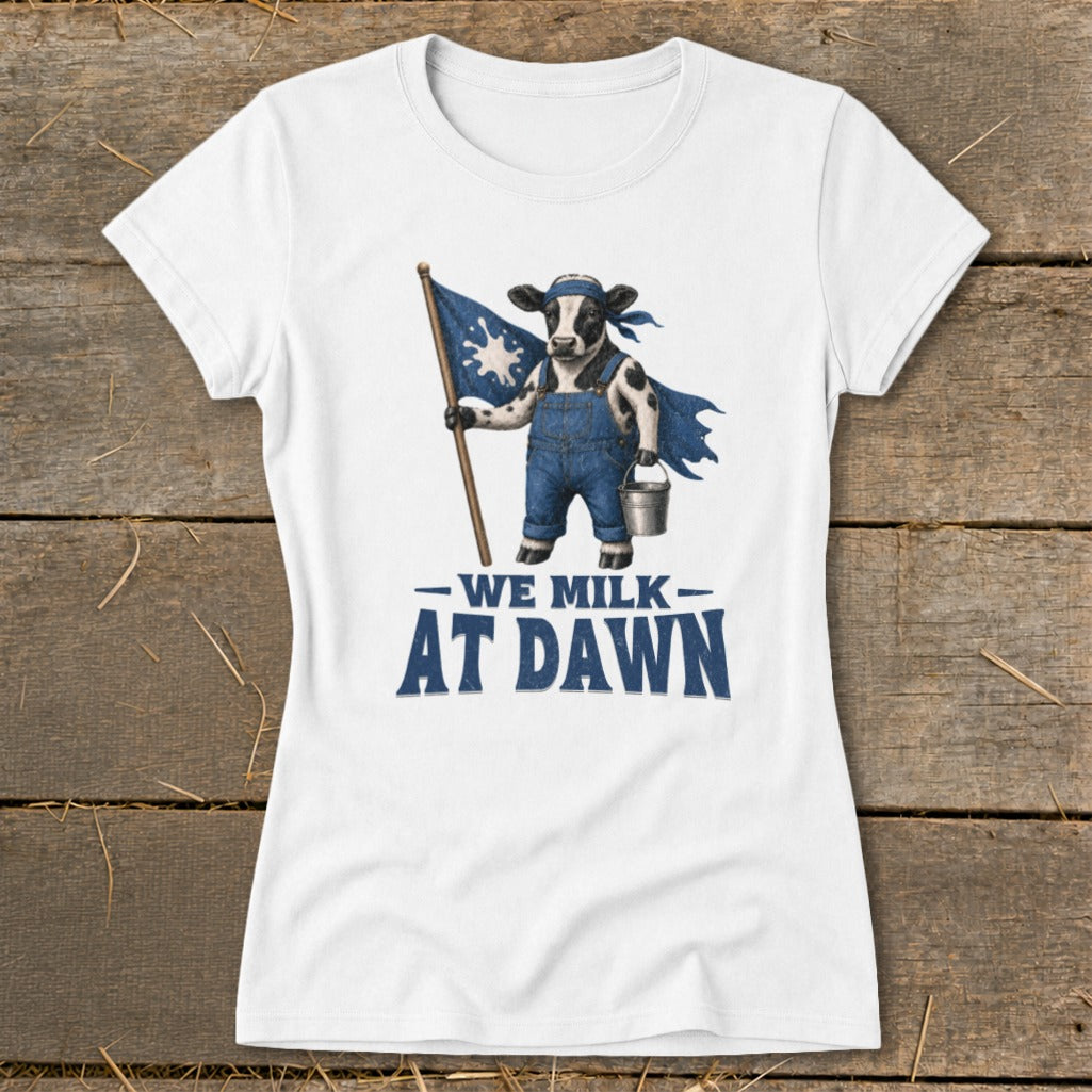 White t-shirt with a cow wearing overalls holding a flag and bucket, reading "We Milk At Dawn."