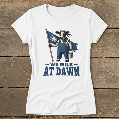 White t-shirt with a cow wearing overalls holding a flag and bucket, reading "We Milk At Dawn."