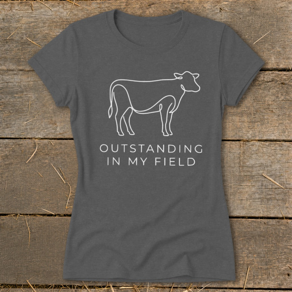 Dark grey t-shirt with white line art cow and text "OUTSTANDING IN MY FIELD".