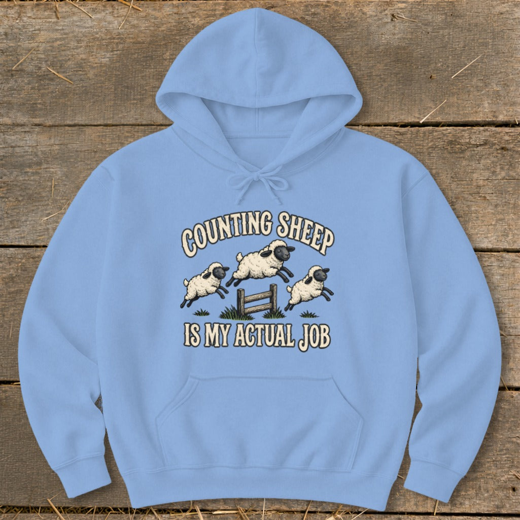 Light blue hoodie with cartoon sheep jumping over a fence and text "COUNTING SHEEP IS MY ACTUAL JOB".