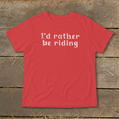 Red t-shirt with white text "I'd rather be riding" on rustic wooden planks.