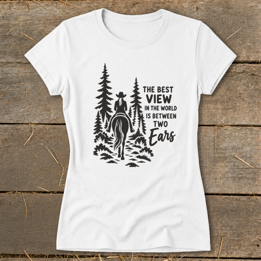A white women's t-shirt features a black graphic of a horseback rider in the woods, with the text "THE BEST VIEW IN THE WORLD IS BETWEEN TWO Ears".