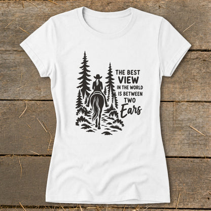 A white women's t-shirt features a black graphic of a horseback rider in the woods, with the text "THE BEST VIEW IN THE WORLD IS BETWEEN TWO Ears".