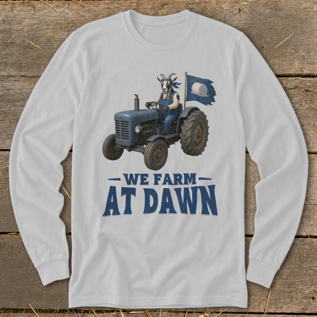 White long-sleeve shirt with a goat driving a blue tractor and flag, reads "We Farm At Dawn."