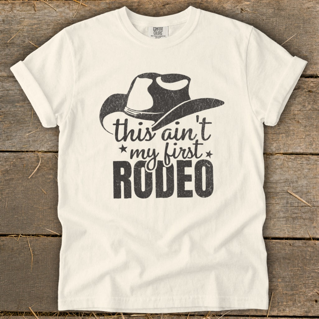 Cream t-shirt with cowboy hat graphic and "this ain't my first RODEO" text.