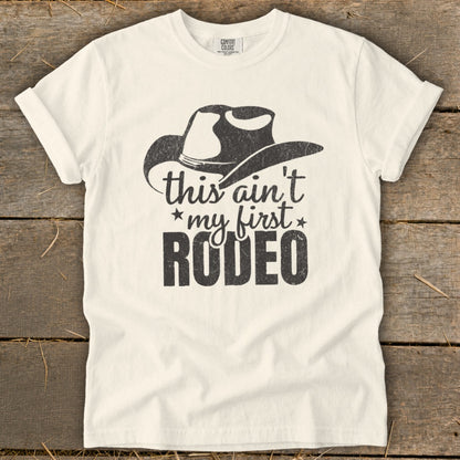 Cream t-shirt with cowboy hat graphic and "this ain't my first RODEO" text.