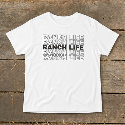 A white short-sleeve t-shirt with five stacked lines of text reading RANCH LIFE on a wooden surface.