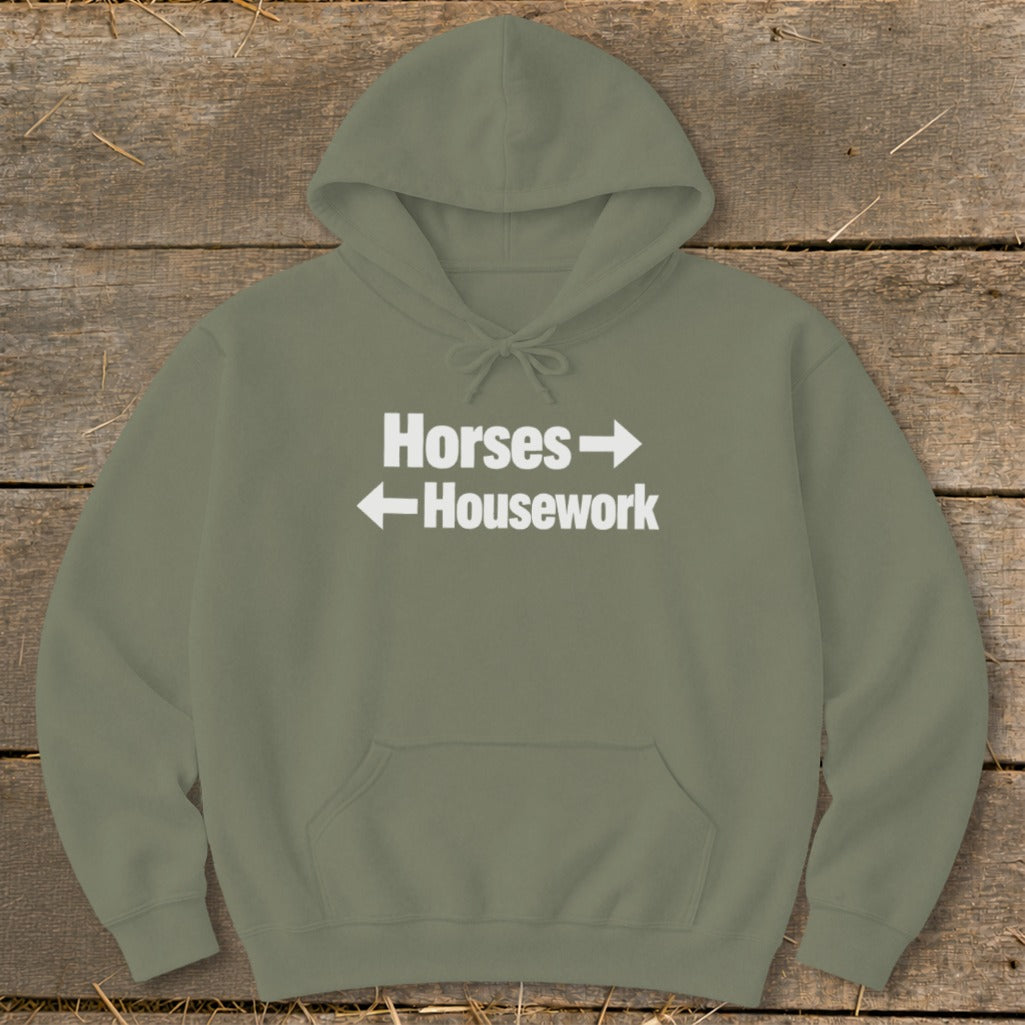 An olive green hooded sweatshirt featuring white text that reads Horses with a right arrow above Housework with a left arrow.