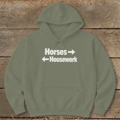 An olive green hooded sweatshirt featuring white text that reads Horses with a right arrow above Housework with a left arrow.