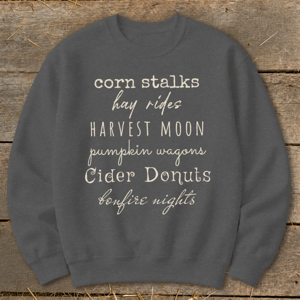 Gray sweatshirt with white text listing "corn stalks, hay rides, harvest moon, pumpkin wagons, Cider Donuts, bonfire nights."