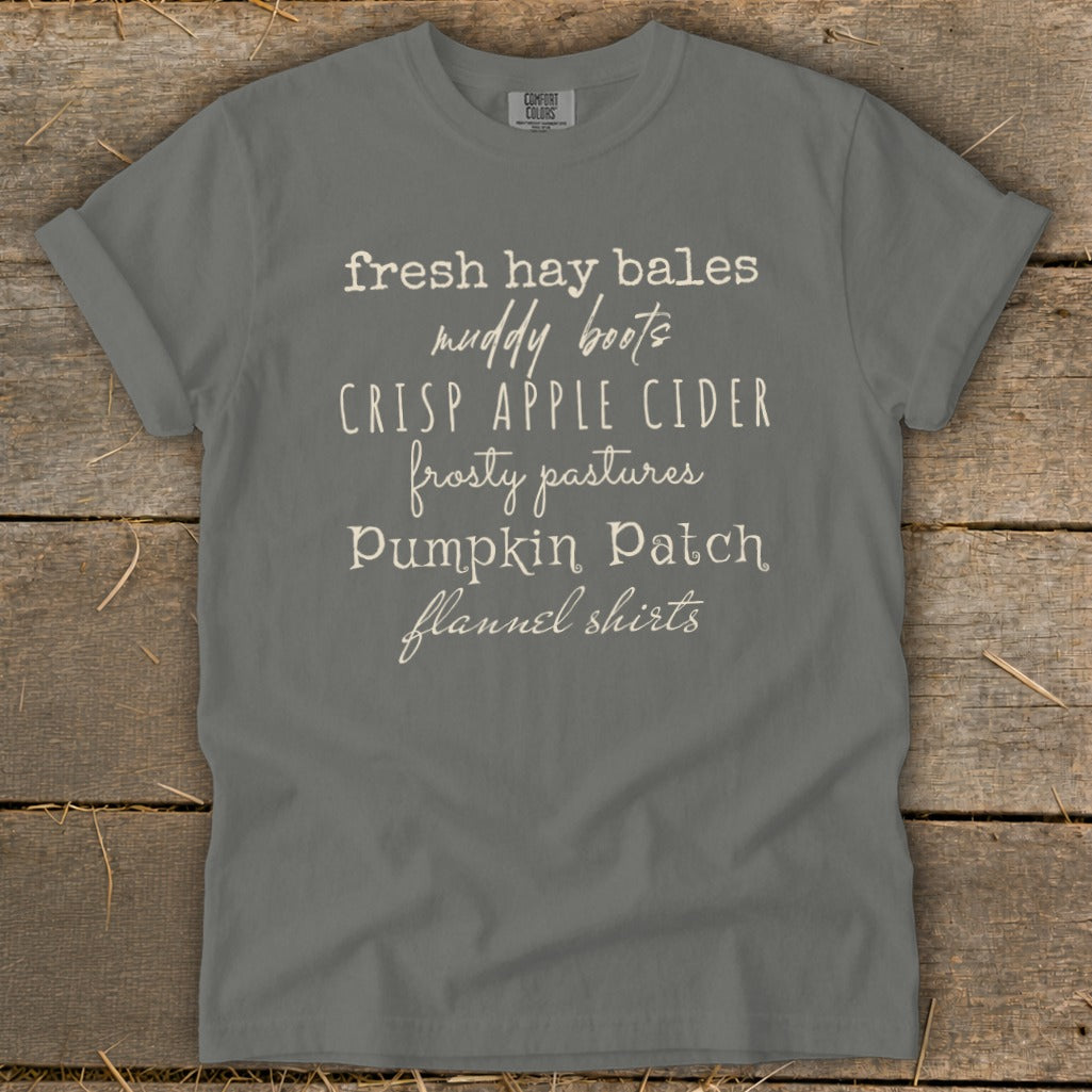 Gray t-shirt with white text listing fall activities: fresh hay bales, muddy boots, crisp apple cider, frosty pastures, pumpkin patch, flannel shirts.