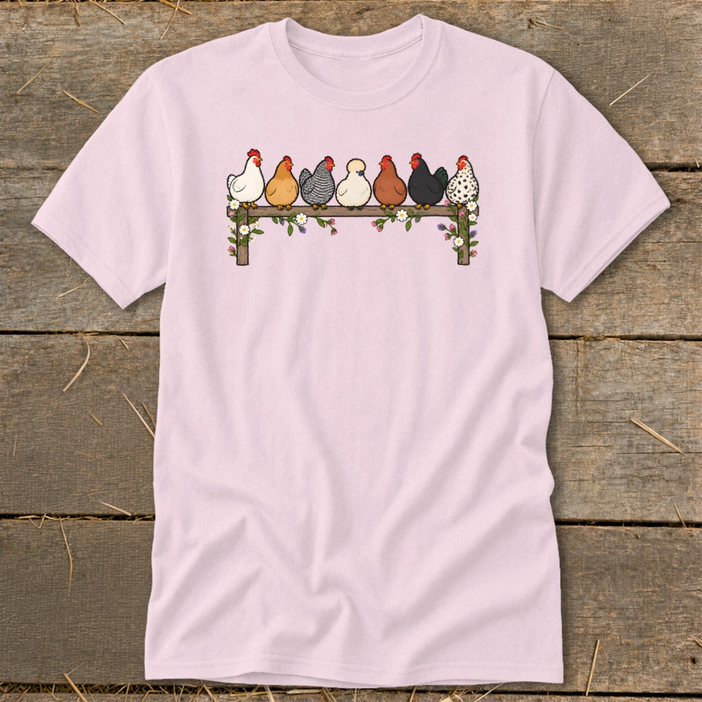 Light pink t-shirt featuring an illustration of seven colorful chickens sitting on a flower-covered wooden fence.