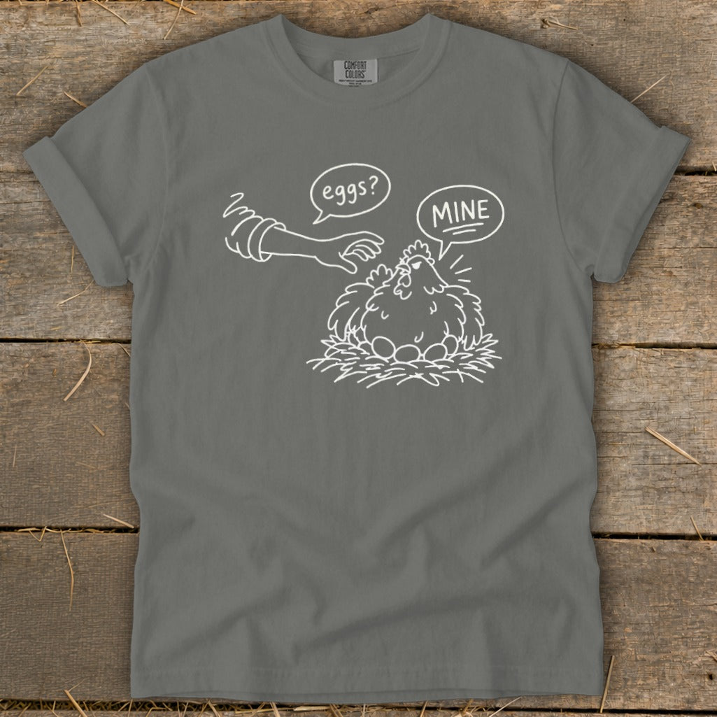 T-shirt with white line drawing of a hand reaching for eggs and a chicken saying "Mine?".