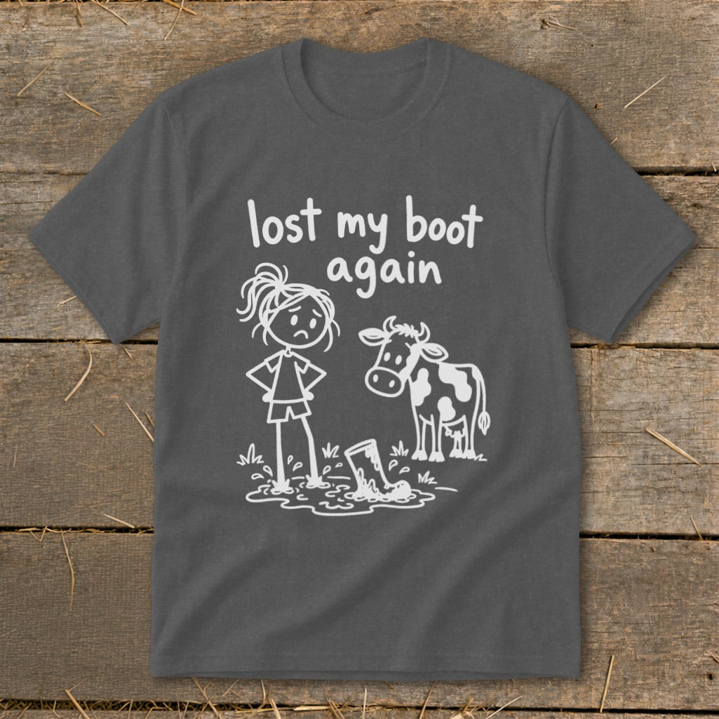 A dark gray t-shirt featuring a white graphic of a frustrated farm girl, a cow, and a muddy boot, with the text "lost my boot again".