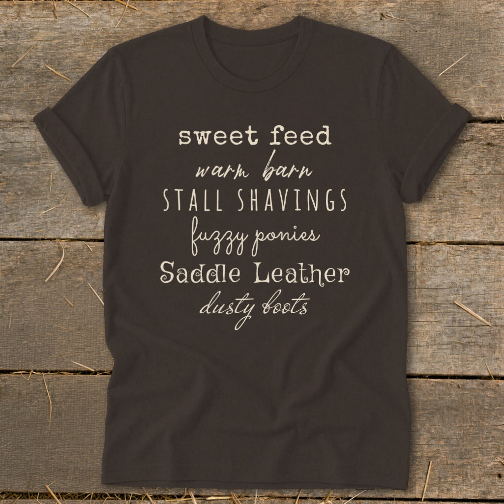 Dark t-shirt with white text listing "sweet feed, warm barn, stall shavings, fuzzy ponies, Saddle Leather, dusty boots."