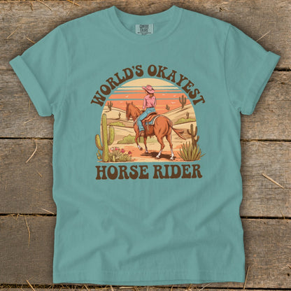 T-shirt graphic with desert scene and text "WORLD'S OKAYEST HORSE RIDER".