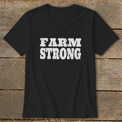 A black V-neck t-shirt lies flat on a wooden background, featuring distressed white text that reads FARM STRONG.