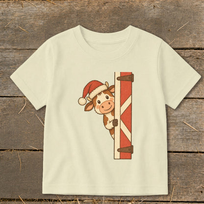 Cream t-shirt with a cartoon cow wearing a Santa hat peeking around a red barn door.