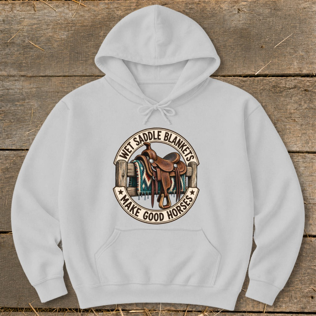 White hoodie with a circular graphic featuring a saddle and text "WET SADDLE BLANKETS MAKE GOOD HORSES".