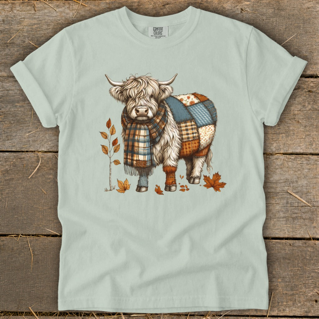 Highland cow with patchwork body and plaid scarf surrounded by autumn leaves.