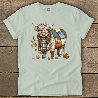 Highland cow with patchwork body and plaid scarf surrounded by autumn leaves.