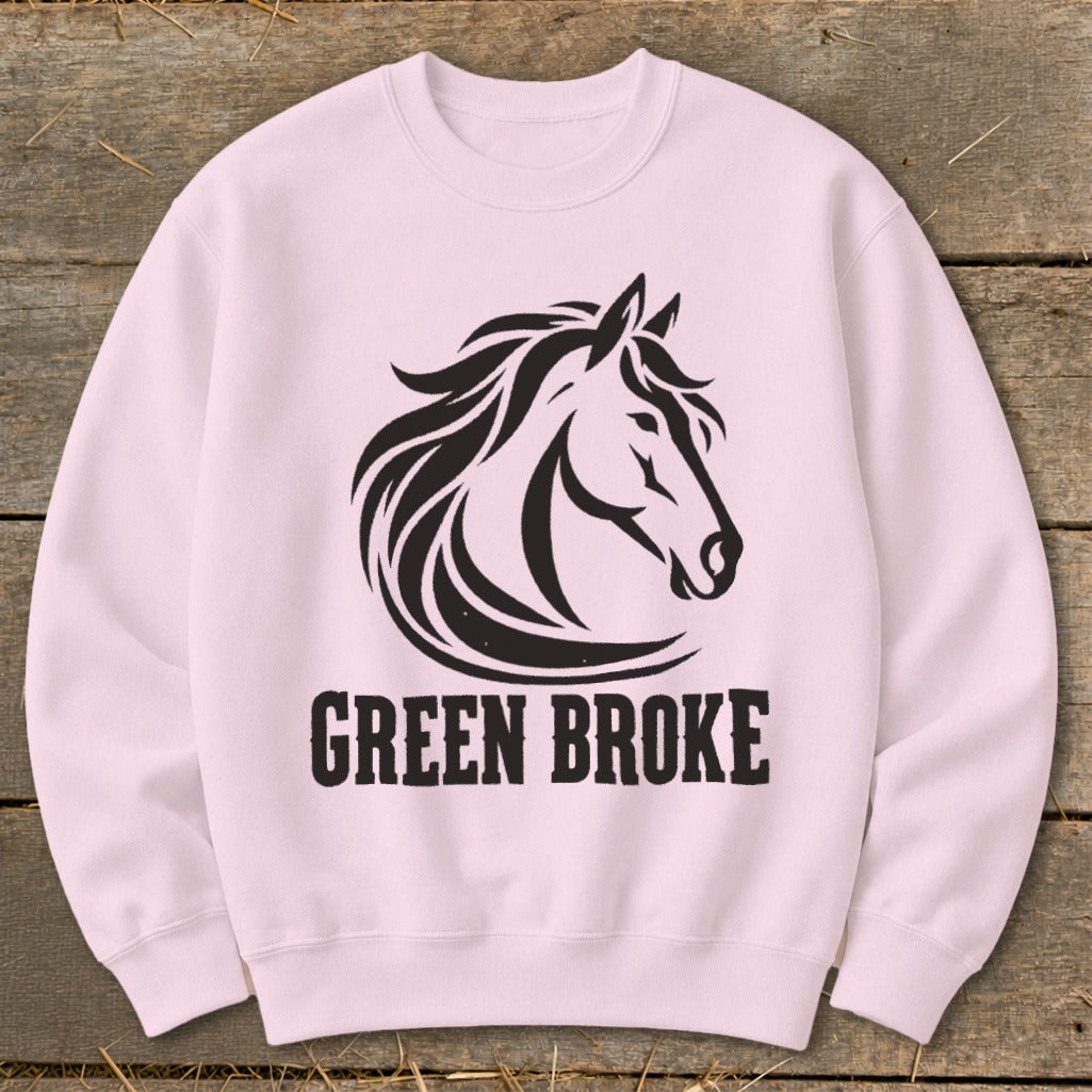 A light pink crewneck sweatshirt featuring a black graphic of a horse head and the text GREEN BROKE on a wooden surface.