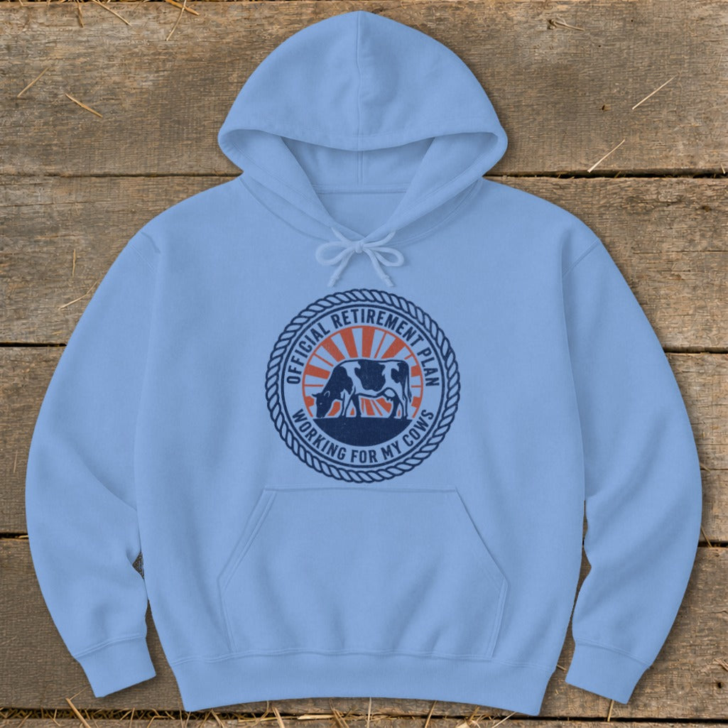Light blue hoodie with a circular graphic featuring a cow and text: "OFFICIAL RETIREMENT PLAN WORKING FOR MY COWS".