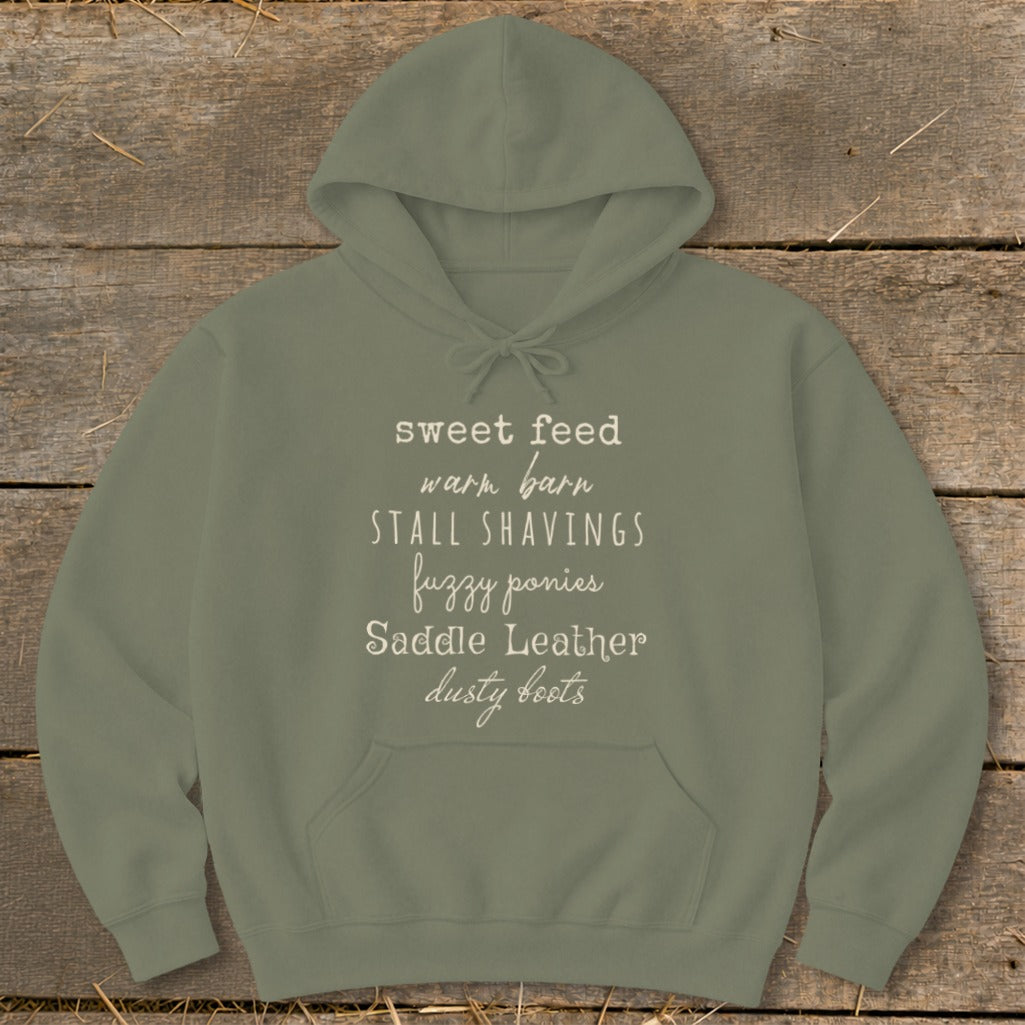 Olive green hoodie with equestrian-themed text: sweet feed, warm barn, stall shavings, fuzzy ponies, saddle leather, dusty boots.