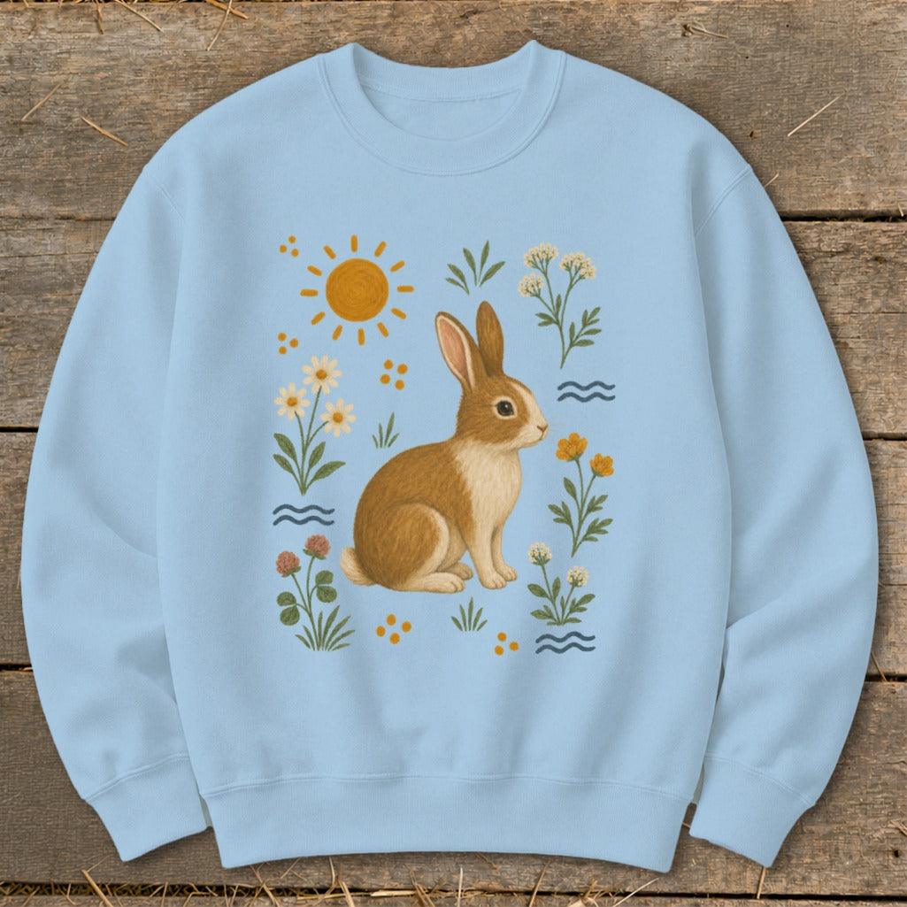 Light blue sweatshirt with a brown and white rabbit surrounded by flowers and a sun.