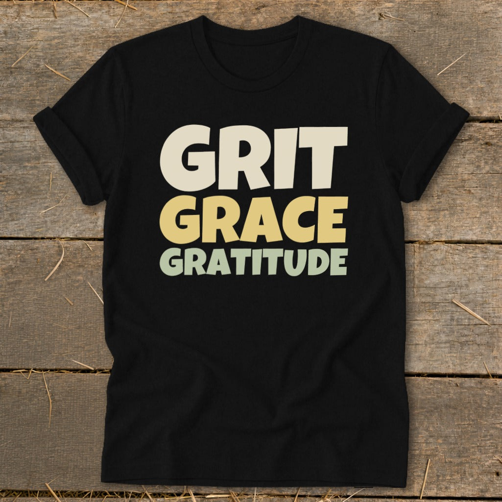 A black short-sleeved t-shirt with the words Grit, Grace, Gratitude printed in stacked, block lettering across the chest.