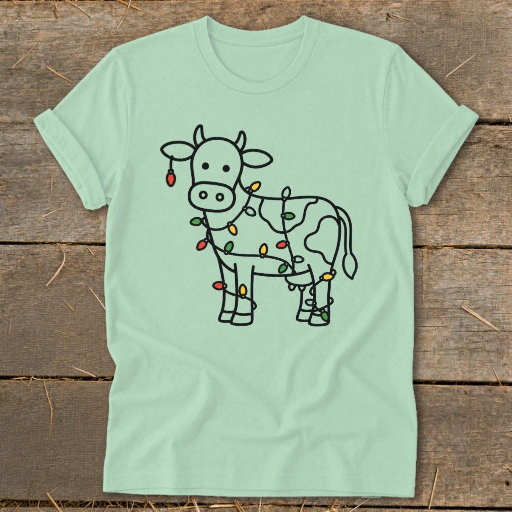 Light green t-shirt with a black outline drawing of a cow wrapped in colorful Christmas lights.