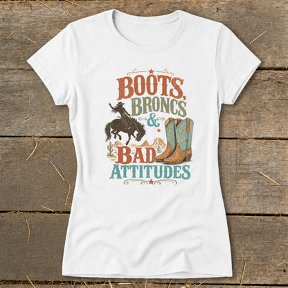 White t-shirt with "Boots Broncs & Bad Attitudes" text, cowboy, and boots graphic.