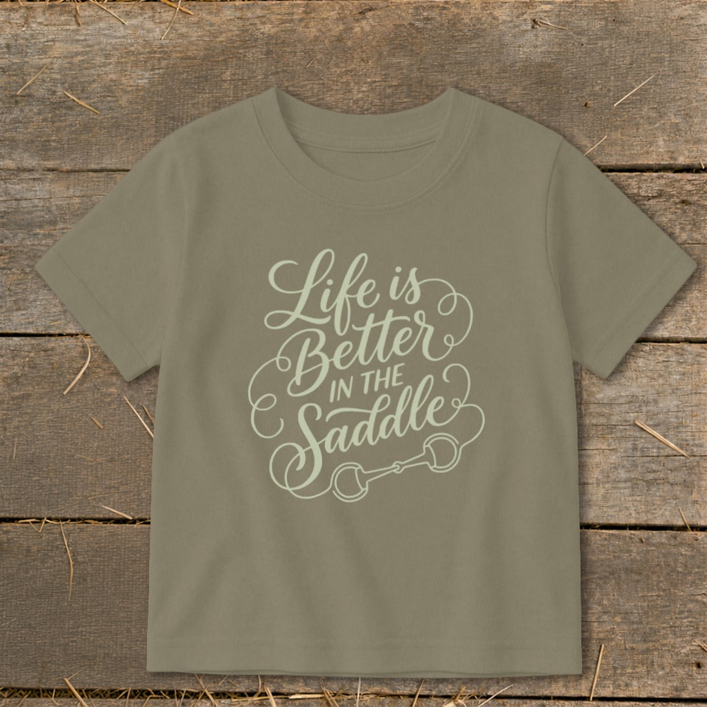 Tan t-shirt with "Life is Better IN THE Saddle" text and horse bit graphic.