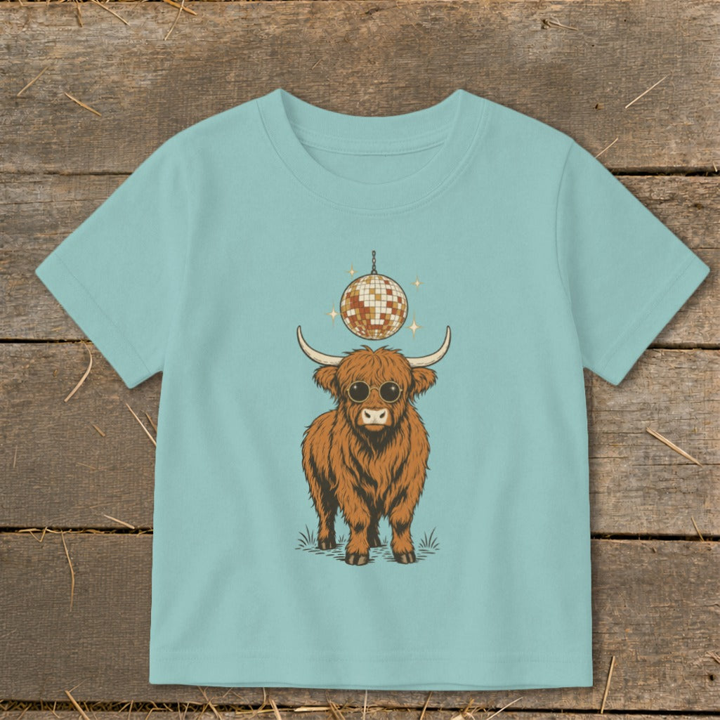 Highland cow with sunglasses and disco ball graphic on a light blue t-shirt.